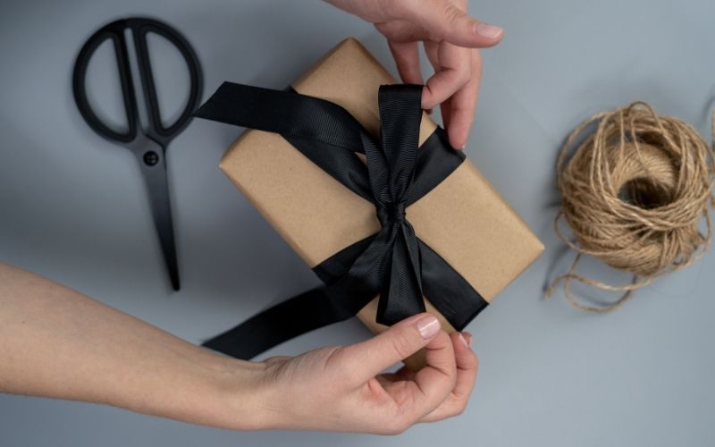 Hands tying a black bow on a box